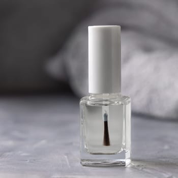 Clear glass refillable bottle with white blank brush cap near grey bath towel on grey close up, cosmetics mockup. Natural skincare nail product, minimal aesthetic