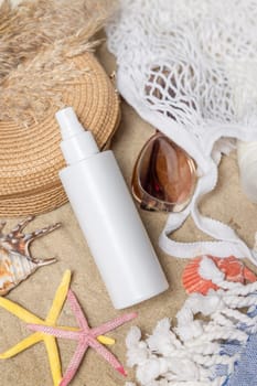 White blank spray bottle, sunglasses, towel, starfishes and shells on a sandy beach, top view. Sunscreen cosmetics mockup. Summer vacation and spf uv-protecting skin care concept