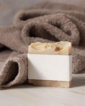 Beige herbal soap bar with blank label near light brown bath towel closeup, packaging mockup, copy space. Natural handmade hygiene soap for daily cleansing and skincare