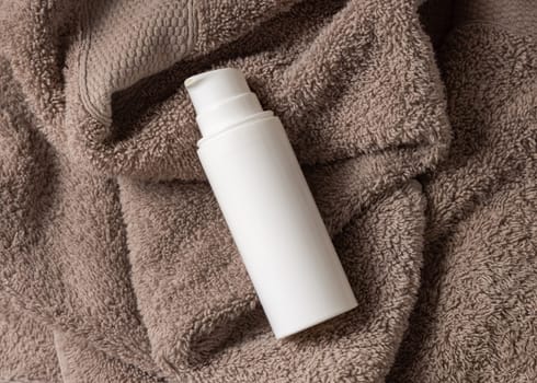 White blank one pump cream bottle on brown towel in bathroom top view, brand packaging mockup. Natural herbal cosmetic product - cream, lotion or foam for daily facecare, copy space