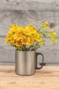 Dandelion bouquet in a metal mug. Vertical. Wood background