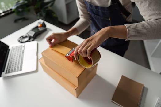 A close-up view of a woman sealing packages with tape in a well-organized workspace, emphasizing her attention to detail and efficiency.