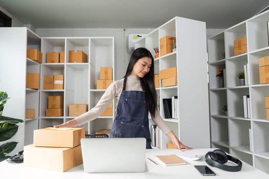 A focused young woman manages logistics in her stylish office, organizing packages while using her computer.