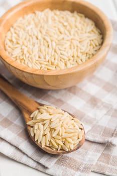 Orzo, kritharaki, risoni pasta. Uncooked dry pasta in spoon on a checkered napkin.