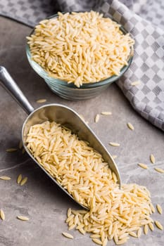 Orzo, kritharaki, risoni pasta. Uncooked dry pasta in scoop on a kitchen table.