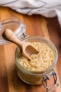 Orzo, kritharaki, risoni pasta. Uncooked dry pasta in jar on a wooden table.