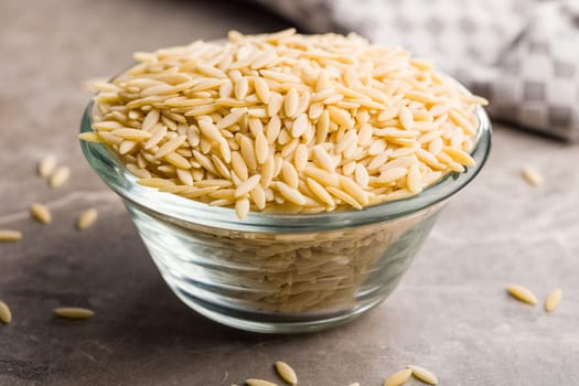 Orzo, kritharaki, risoni pasta. Uncooked dry pasta in bowl on a kitchen table.