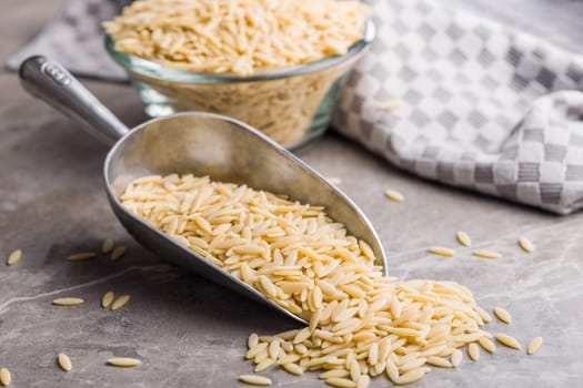 Orzo, kritharaki, risoni pasta. Uncooked dry pasta in scoop on a kitchen table.