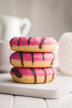 Sweet pink donut with chocolate strips on a white table.