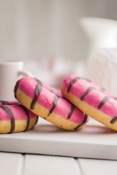 Sweet pink donut with chocolate strips on a white table.