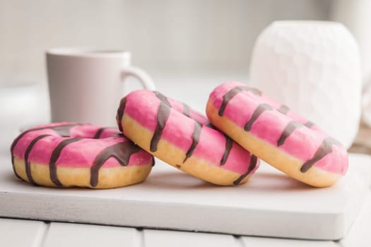 Sweet pink donut with chocolate strips on a white table.