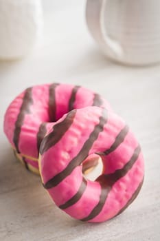 Sweet pink donut with chocolate strips on a kitchen table.
