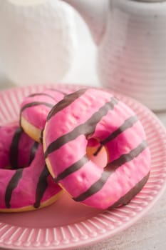 Sweet pink donut with chocolate strips on plate on a kitchen table.