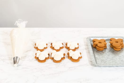 Gingerbread cookies await their second halves on a marble surface, each meticulously piped with buttercream to craft delightful sandwich treats. The precision of the piping adds a festive touch.