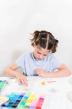 Little girl enjoys crafting colorful bracelets with vibrant clay beads set.