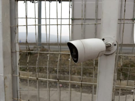 CCTV camera on fencing to ensure safety on street. Security equipment for monitoring crime on street. Ensuring security and control using surveillance camera, close up photo