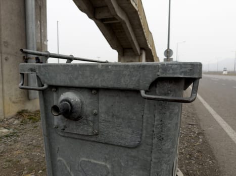 Metal trash can on street along road for waste collection. Steel bin on wheels for collecting garbage. Close up photo of standard trash can body