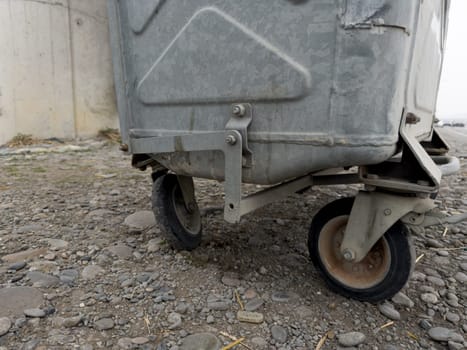 Wheels of old trash can on street. The concept of collecting garbage in specialized container on street for waste recycling. Old gray trash can, cleanliness in city