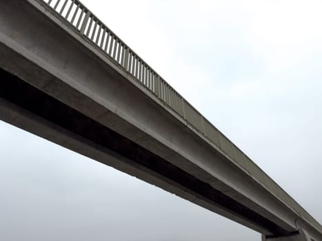 Concrete pedestrian bridge against gray sky. Gloomy gray bridge for crossing road or river on cloudy day. Atmospheric old bridge for people on empty sky background. Photo below bridge