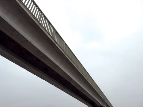 Long concrete bridge against dark sky. Cloudy day with footbridge across road for pedestrians. Simple concrete pedestrian bridge design made of concrete blocks and metal fencing for safety