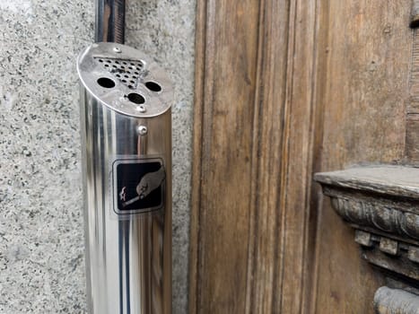Steel outdoor ashtray for heavy smokers. Convenient ashtray is located at entrance to building. Trash of cigarette butts after smoking on street. Cigarette icon on metal ashtray in smoking area