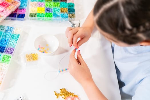 Little girl enjoys crafting colorful bracelets with vibrant clay beads set.