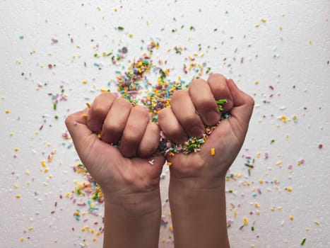 Child's hands clenched into fists with sugar confectionery sprinkles on white background.