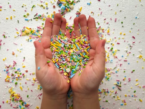 Close-up of child's hands playing with colorful sprinkles on table.