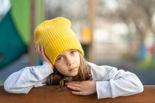 Serious girl in yellow cap with freckles looking at camera, with hand on head in closeup portrait. Intense gaze and neutral expression highlighting features