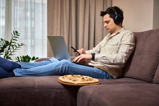 freelancer man using smart phone and laptop on sofa at home, work from home