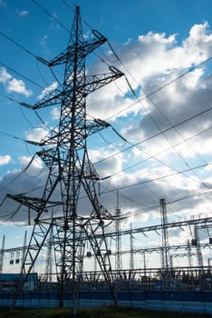 A large electrical power substation with towering transmission lines and metal structures, supplying energy under a partly cloudy sky.