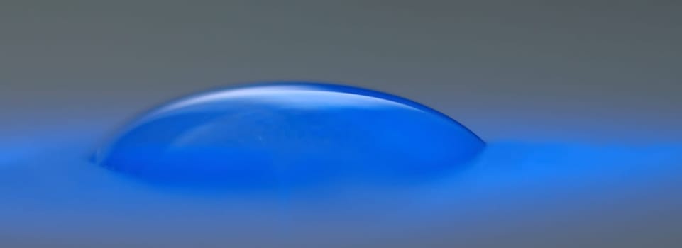 A drop of water on a sheet of paper is just sucking in and is brightened by a blue light-emitting diode.