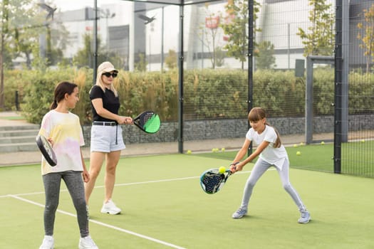 Cheerful coach teaching child to play tennis while both standing on tennis court. High quality photo