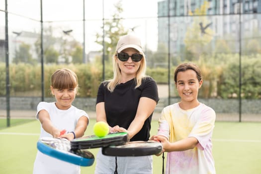Young sporty woman with children playing padel game in court on sunny day. High quality photo