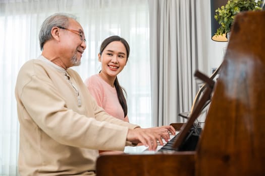 Family. Young woman teaching piano for senior man teaching, happy daughter and elderly father with eyeglasses relaxation playing piano together in living room at home, lifestyle life after retirement