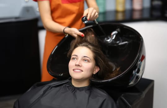 Master washes her hair in sink for client in hairdressing salon. Services of beauty salons and hairdressing salons concept