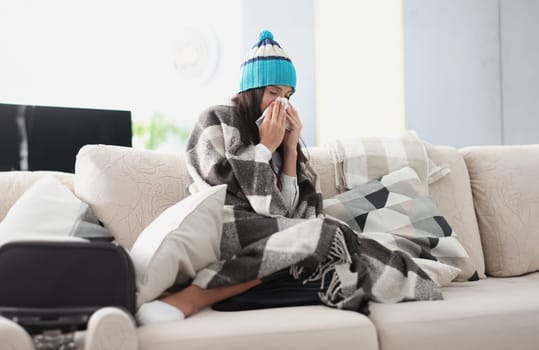 chilled woman on sofa in blanket and hat holds handkerchief. Seasonal colds concept
