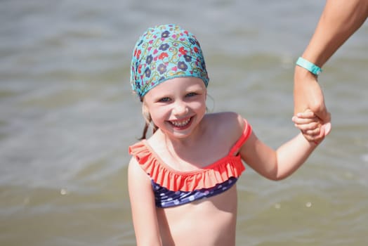 Smiling little girl in swimsuit and a scarf at sea. Rules for finding children in the sun concept