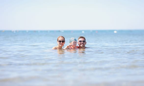 Man, woman and child swim in sea. Family travel with kids concept