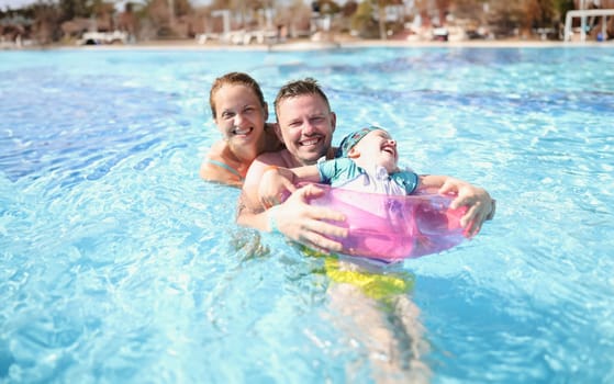 Family mom dad and daughter laugh and swim in pool. Travel and vacation with children concept