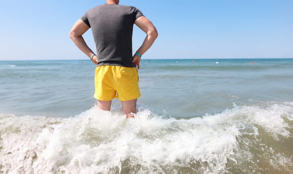 Man in yellow shorts stands knee-deep in sea. Lifeguard work at sea concept