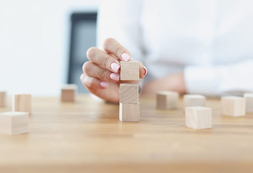 Female hand builds tower from wooden cubes. Building service business from scratch to market dominance concept