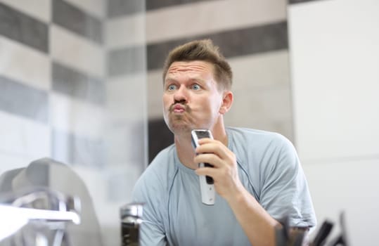 Man in front of a mirror shaves off his stubble with machine. How to properly shave off facial stubble concept