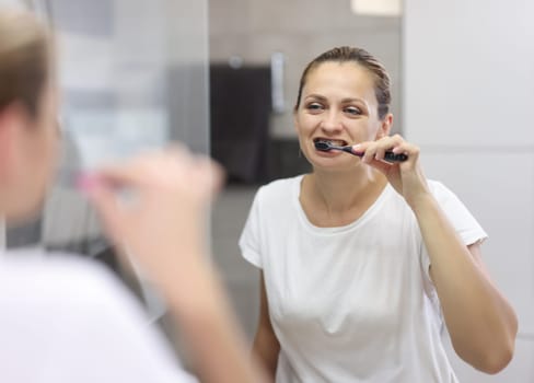 Woman brushes her teeth in bathroom in front of mirror. Morning oral hygiene concept