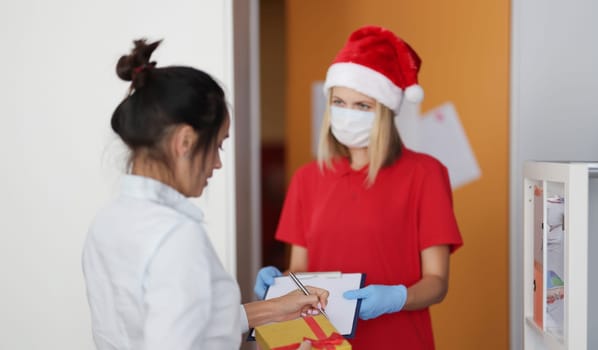 Woman courier in protective medical mask and gloves delivers parcel. Safe supply of dovars in the coronavirus pandemic concept