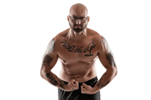 Handsome bald, bearded, tattooed male in glasses, black shorts is posing and showing his muscles isolated on white background, looking at the camera. Chic muscular body, fitness, gym, healthy lifestyle concept. Close-up portrait.