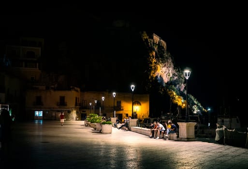 A group of people sitting on a bench at night. Photo of people enjoying a peaceful evening on a bench in Sicily's Eolie Islands