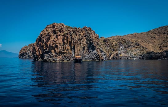 A small boat in the middle of a body of water. Photo of a serene boat floating in the crystal clear waters of Sicily's Eolie Islands