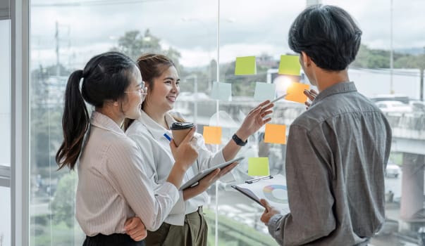 team employees busy brainstorming develop business ideas write on colorful sticky notes, concentrated colleagues share thoughts on pads on glass window.