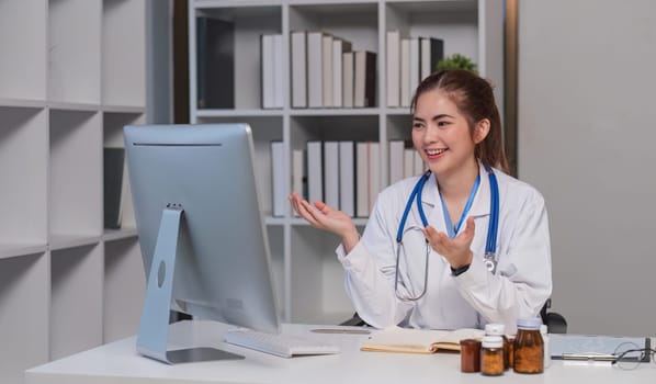 Beautiful Asian doctor smiling using laptop computer explaining detailed medical information online at hospital health medical concept..